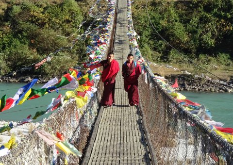 Zwei Mönche auf einer von Gebetsfahnen gezierten Hängebrücke bei Punakha